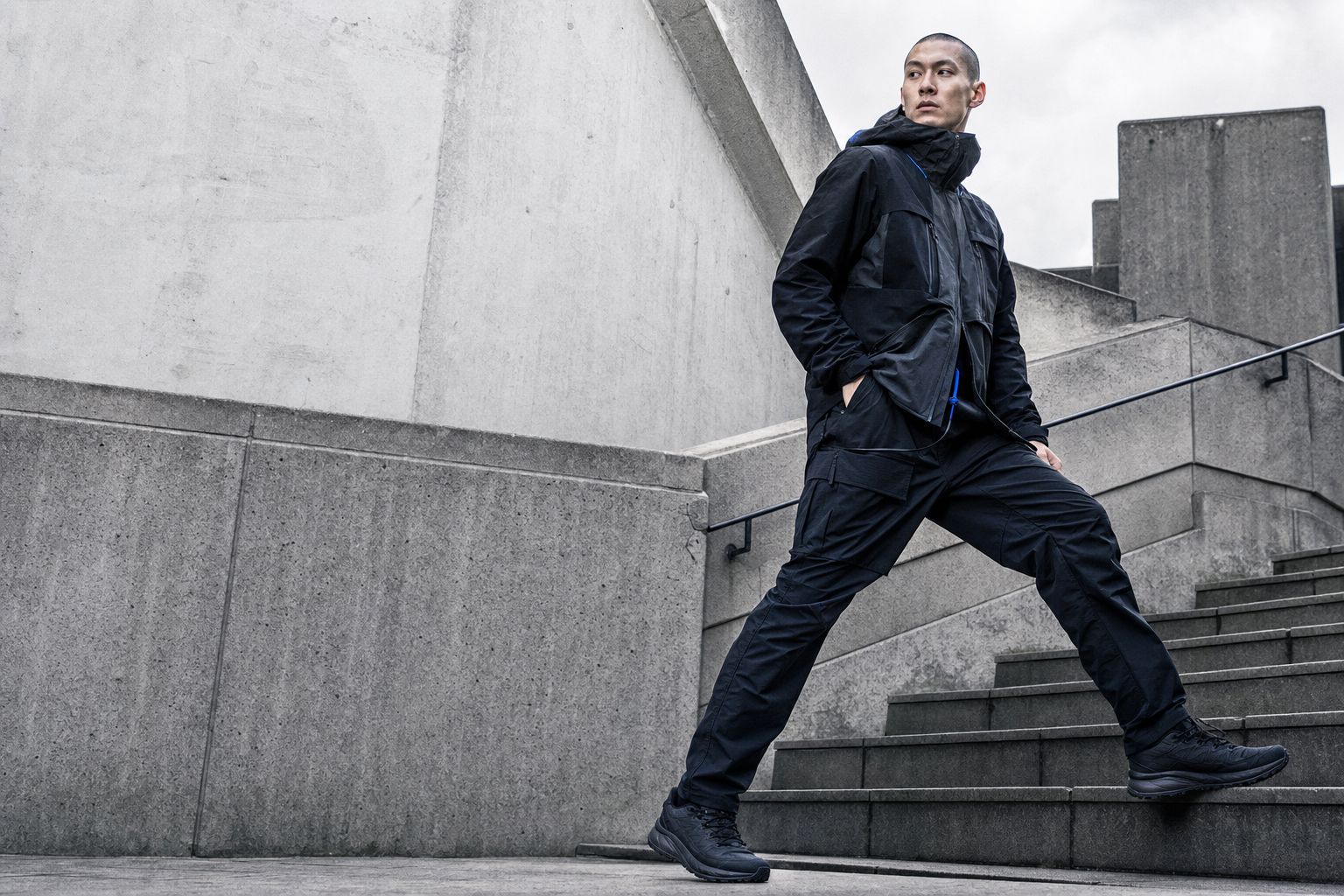 Model in technical black streetwear moving through brutalist architecture